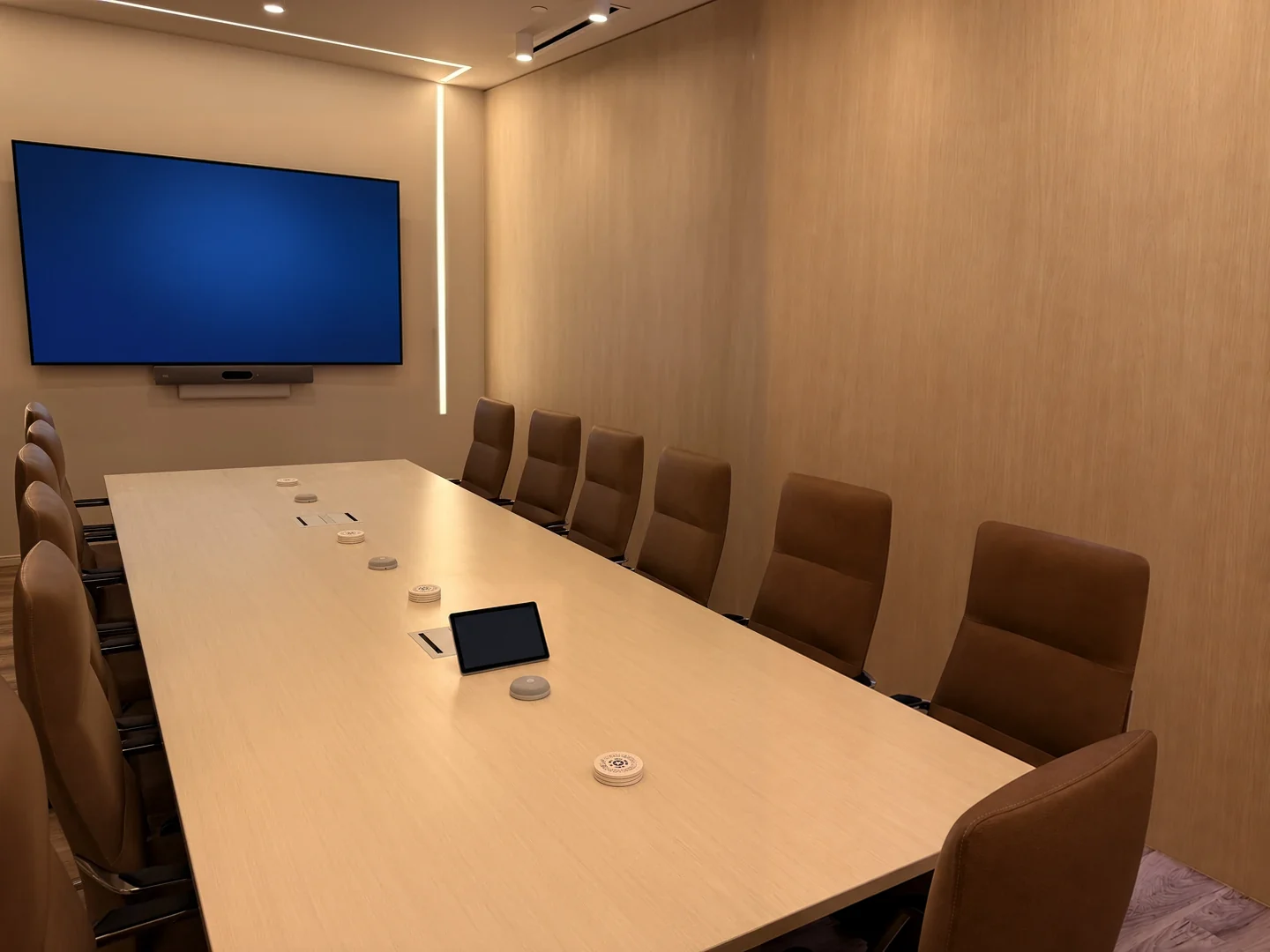 The conference room with a long meeting table, wall-mounted display, video conferencing and table microphones.
