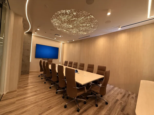 Wide view of the conference room with a large wall display and warm wood paneling.